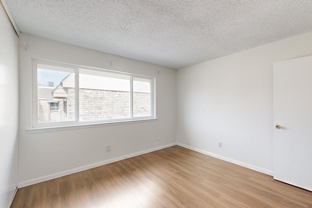 spare room featuring light wood-type flooring, a textured ceiling, and baseboards