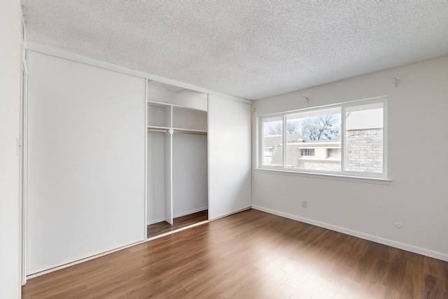 unfurnished bedroom featuring a textured ceiling, a closet, and dark wood finished floors