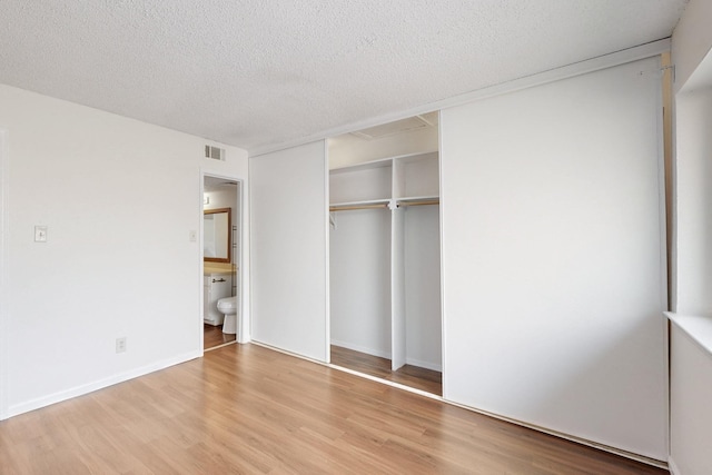 unfurnished bedroom with visible vents, connected bathroom, wood finished floors, a textured ceiling, and a closet