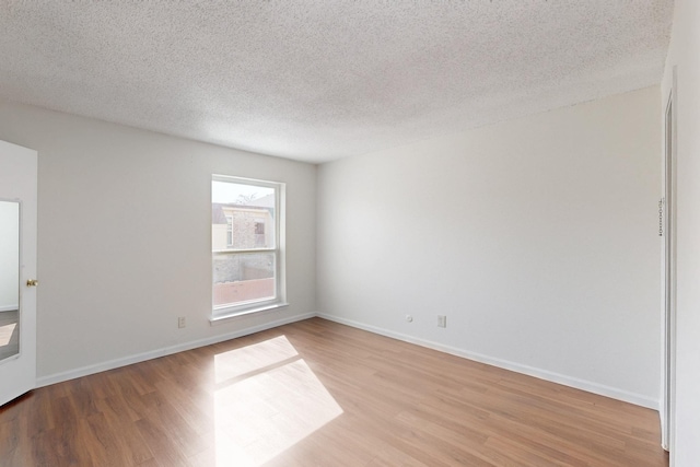 spare room with a textured ceiling, light wood-style flooring, and baseboards