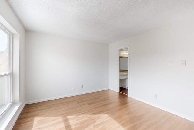 unfurnished room featuring a textured ceiling, baseboards, and light wood-style floors