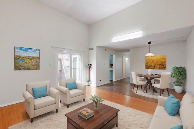 living area with a towering ceiling, wood finished floors, visible vents, and baseboards