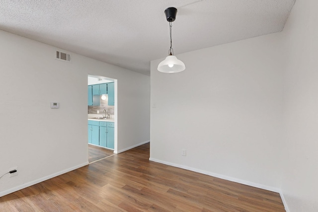 spare room with a sink, wood finished floors, visible vents, and baseboards