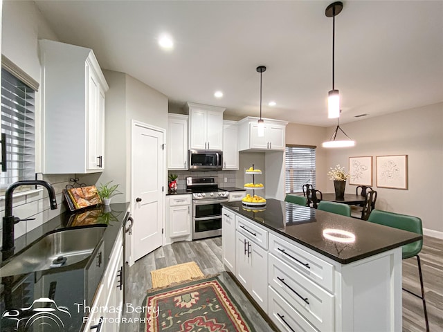 kitchen featuring sink, white cabinetry, a center island, hanging light fixtures, and stainless steel appliances