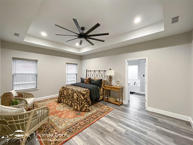 bedroom with ceiling fan, a tray ceiling, and hardwood / wood-style floors