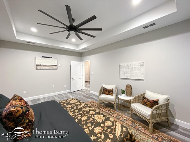 bedroom with ceiling fan, dark hardwood / wood-style floors, and a raised ceiling