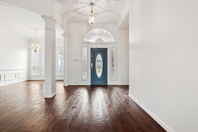 foyer entrance featuring crown molding, a notable chandelier, dark wood-type flooring, and ornate columns