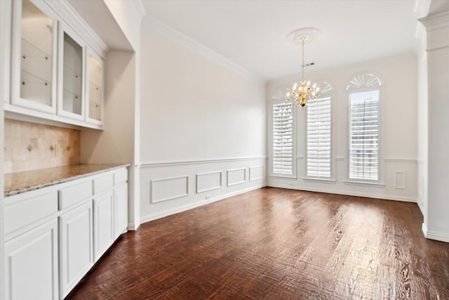 unfurnished dining area featuring dark hardwood / wood-style flooring, crown molding, and a chandelier