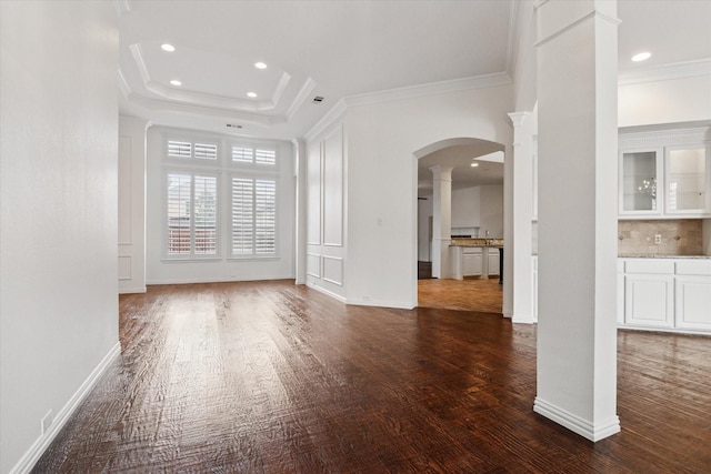 unfurnished living room featuring ornamental molding, dark hardwood / wood-style flooring, a raised ceiling, and decorative columns