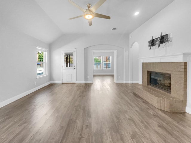 unfurnished living room with wood finished floors, a brick fireplace, visible vents, and a healthy amount of sunlight