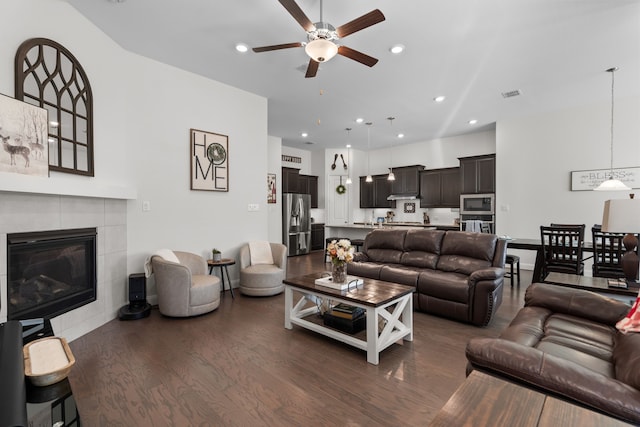 living room with dark wood-type flooring, a tile fireplace, and ceiling fan