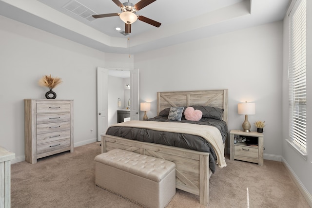 bedroom with light colored carpet, ceiling fan, and a tray ceiling