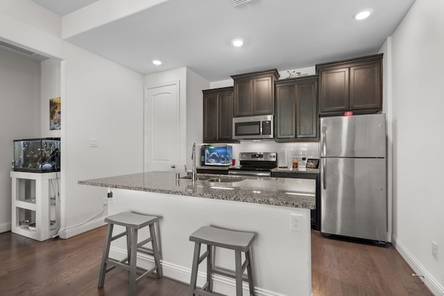 kitchen with dark brown cabinetry, stainless steel appliances, dark stone countertops, and a center island with sink