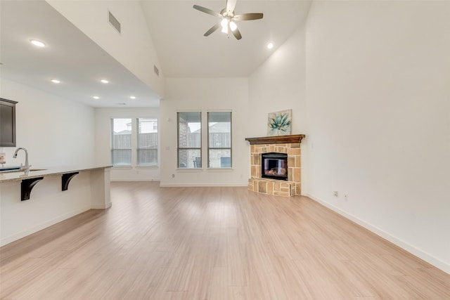 living room with a fireplace, high vaulted ceiling, ceiling fan, and light wood-type flooring