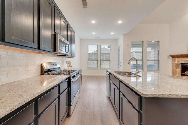 kitchen featuring sink, light stone counters, appliances with stainless steel finishes, a kitchen island with sink, and backsplash