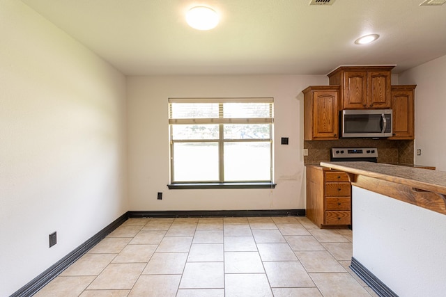 19482 Ruggles Ct, Flint, TX 75762 - kitchen with appliances with stainless steel finishes, brown cabinets, decorative backsplash, light tile patterned floors, and baseboards