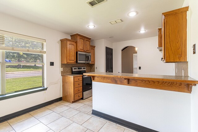 19482 Ruggles Ct, Flint, TX 75762 - kitchen featuring appliances with stainless steel finishes, a peninsula, decorative backsplash, arched walkways, and brown cabinetry