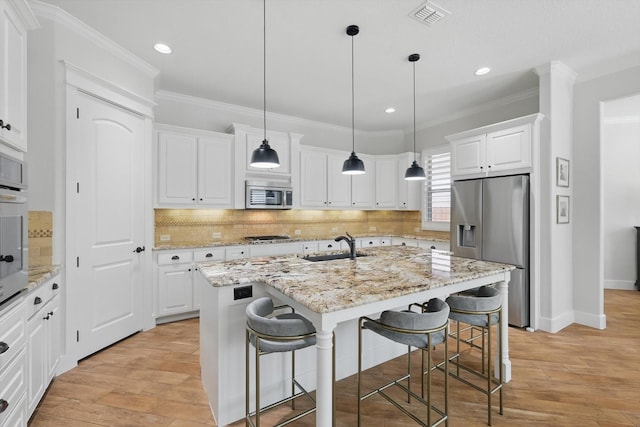 kitchen featuring a center island with sink, visible vents, appliances with stainless steel finishes, a kitchen breakfast bar, and white cabinetry