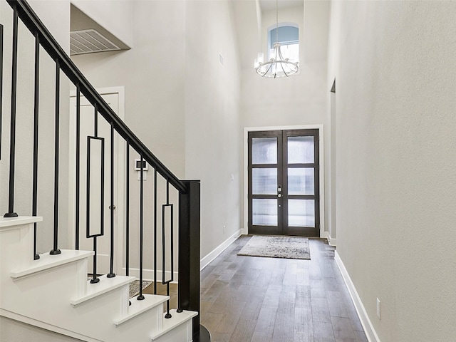 entryway featuring french doors, wood-type flooring, a notable chandelier, and a towering ceiling