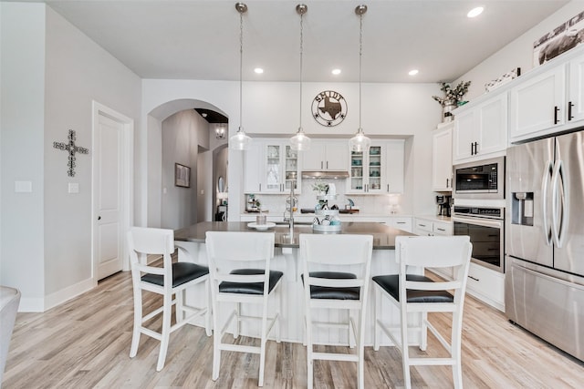 kitchen featuring white cabinets, an island with sink, glass insert cabinets, decorative light fixtures, and stainless steel appliances