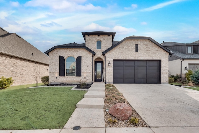 french provincial home with an attached garage, concrete driveway, brick siding, and a front yard