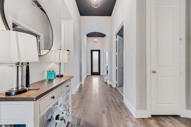 corridor featuring light wood-style flooring, arched walkways, and baseboards