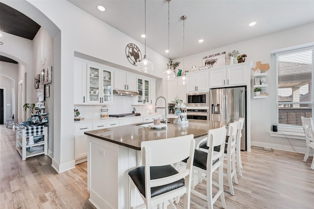 kitchen featuring arched walkways, a kitchen island with sink, glass insert cabinets, and white cabinetry