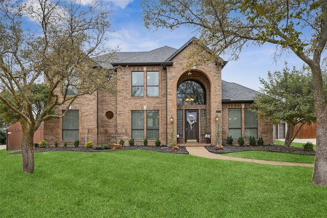 traditional home featuring a shingled roof, brick siding, and a front lawn