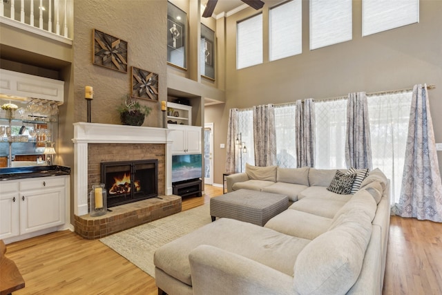 living area featuring built in shelves, a fireplace, a towering ceiling, light wood-style floors, and wet bar