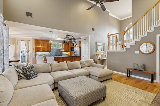 living room featuring baseboards, a towering ceiling, ornamental molding, stairs, and light wood-style floors