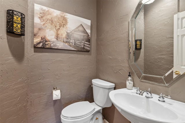 bathroom with a textured wall, a sink, and toilet