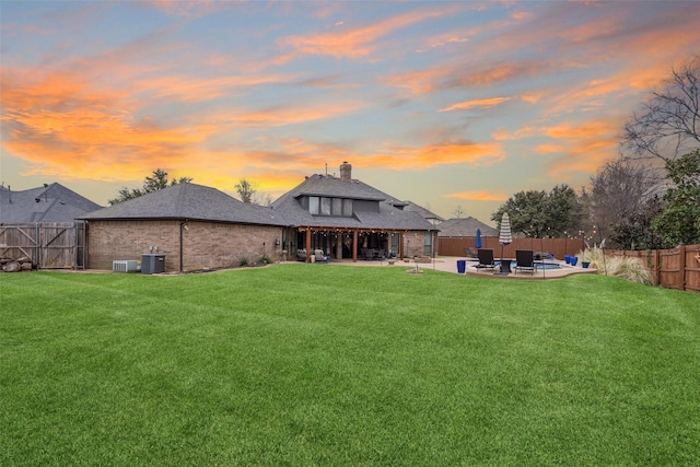 back of house at dusk featuring a fenced backyard, a lawn, central AC, and a patio