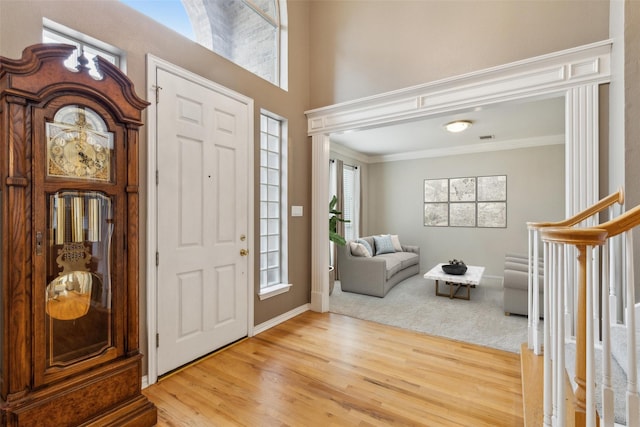 foyer with baseboards, visible vents, a towering ceiling, ornamental molding, and wood finished floors