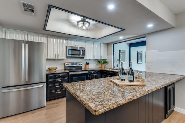 kitchen with white cabinetry, appliances with stainless steel finishes, kitchen peninsula, and a raised ceiling