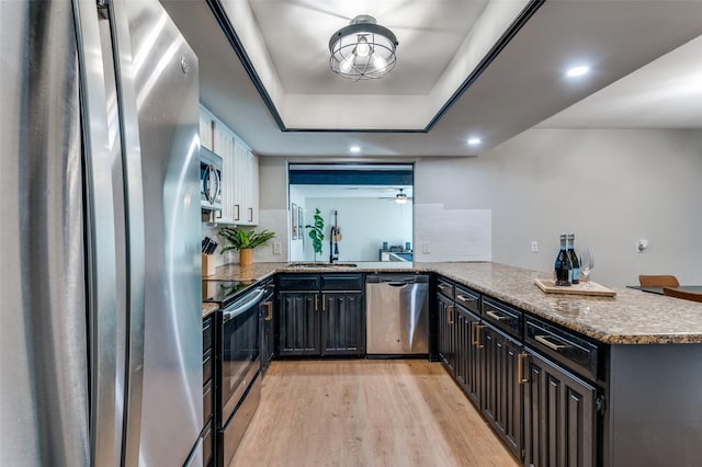 bar featuring appliances with stainless steel finishes, sink, decorative backsplash, a raised ceiling, and light hardwood / wood-style flooring