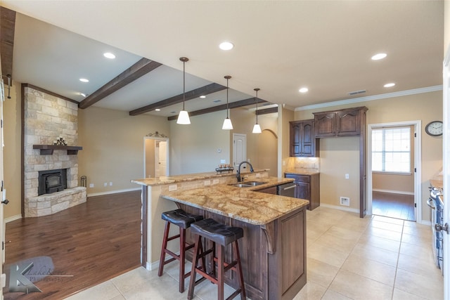 kitchen with sink, a breakfast bar, light stone countertops, decorative light fixtures, and a large island with sink