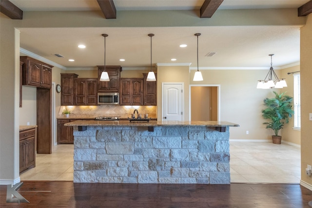 kitchen with dark brown cabinetry, an island with sink, hanging light fixtures, and backsplash