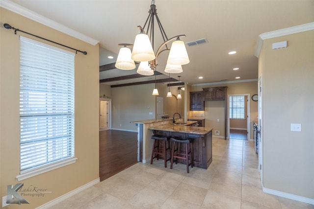 kitchen with sink, a breakfast bar area, ornamental molding, pendant lighting, and light stone countertops