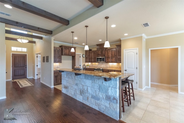 kitchen with appliances with stainless steel finishes, a spacious island, light stone counters, decorative backsplash, and beamed ceiling