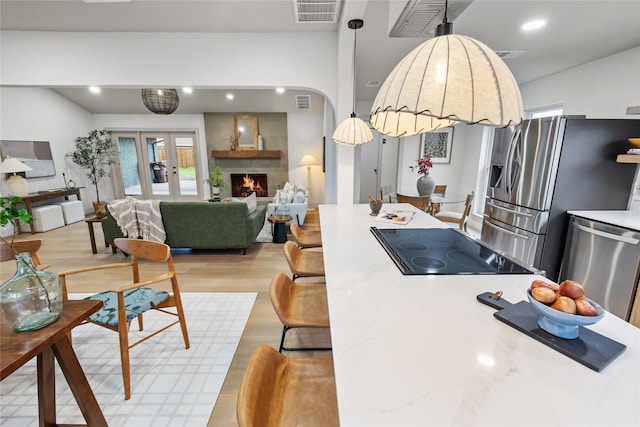 kitchen featuring french doors, appliances with stainless steel finishes, a fireplace, and light hardwood / wood-style floors