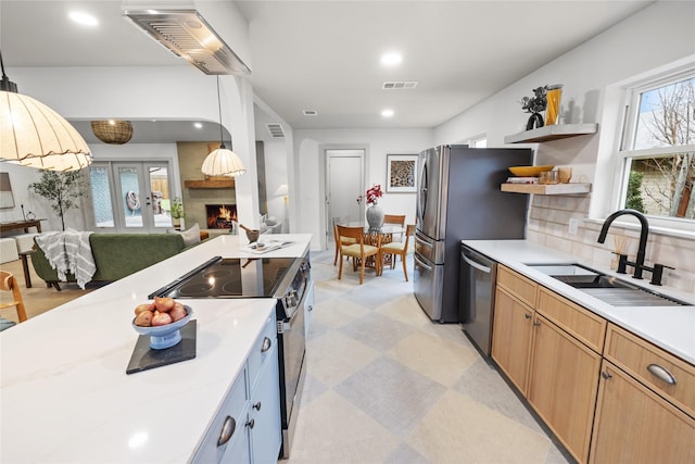 kitchen with pendant lighting, sink, appliances with stainless steel finishes, a large fireplace, and french doors