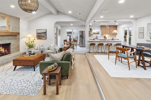 living room featuring vaulted ceiling with beams, a fireplace, and light wood-type flooring