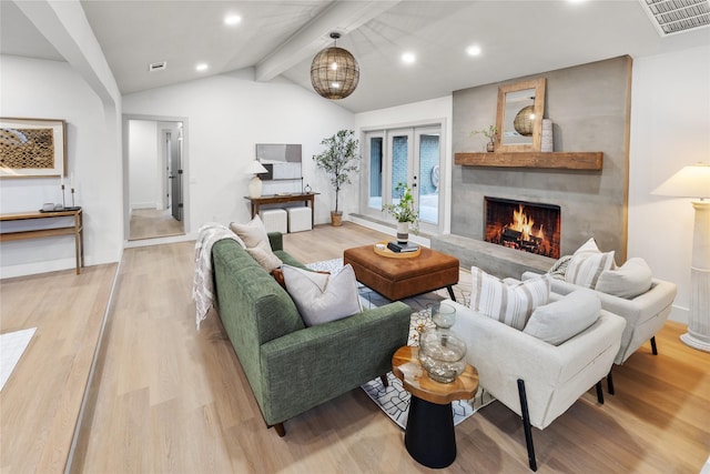 living room with vaulted ceiling with beams, a large fireplace, light hardwood / wood-style floors, and french doors