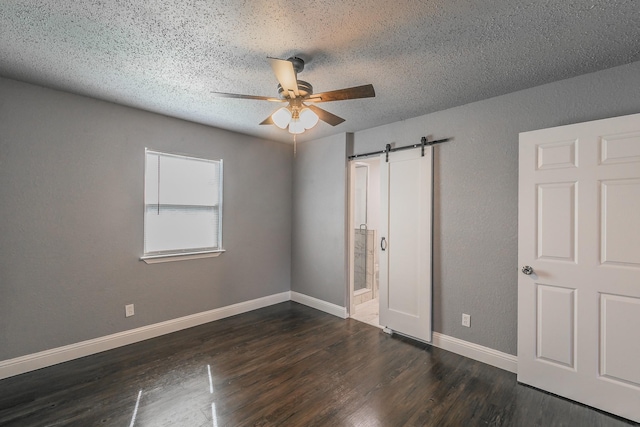 unfurnished bedroom featuring dark hardwood / wood-style floors, ensuite bath, ceiling fan, a barn door, and a textured ceiling