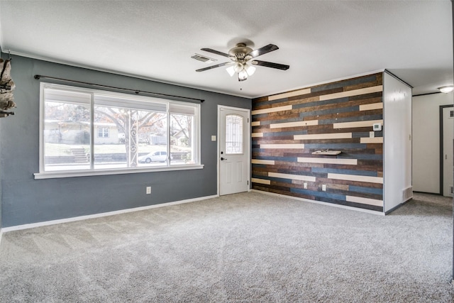 carpeted empty room featuring ceiling fan, wooden walls, and a textured ceiling