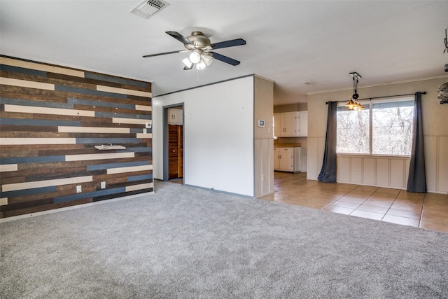 unfurnished living room featuring ceiling fan, crown molding, light carpet, and wooden walls