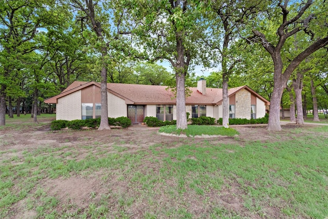 mid-century modern home featuring brick siding, a chimney, and a front yard