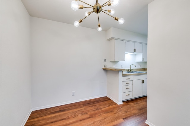 kitchen with white cabinetry, an inviting chandelier, sink, and hardwood / wood-style floors