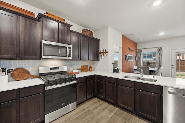 kitchen with sink, tasteful backsplash, dark brown cabinets, light wood-type flooring, and appliances with stainless steel finishes