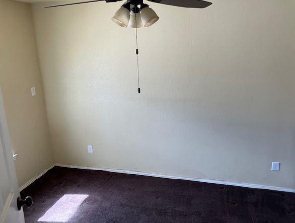 unfurnished room with dark colored carpet and ceiling fan